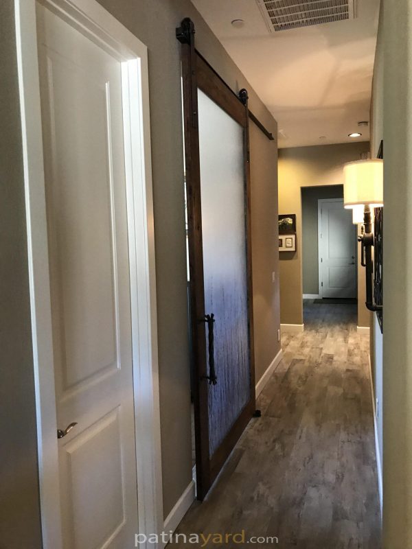 Stained mesquite wood barn door with a 3form resin panel and twig style handle in a hallway