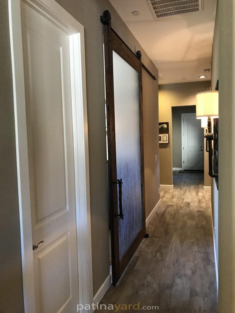 Stained mesquite wood barn door with a 3form resin panel and twig style handle in a hallway