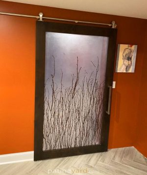 Dark stained wood barn door with a 3form birch branch resin panel against an orange wall