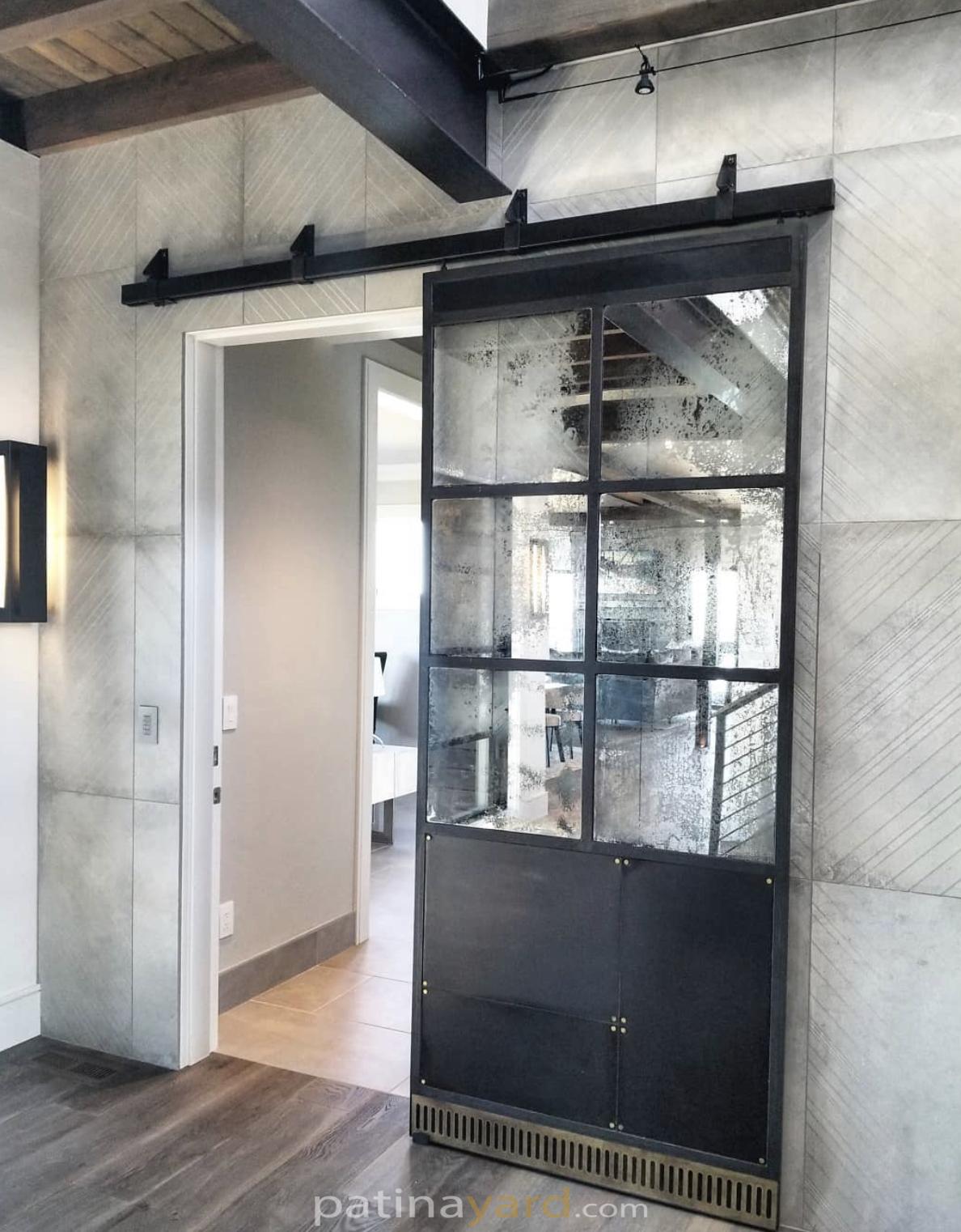 warehouse style barn door with antique mirrors and a metal panel tow kick with brass rivets and accent piece on the bottom