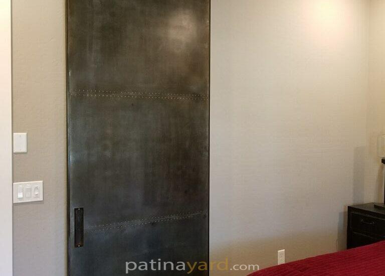 Steel panel barn door with rivets in the seams and patina finish