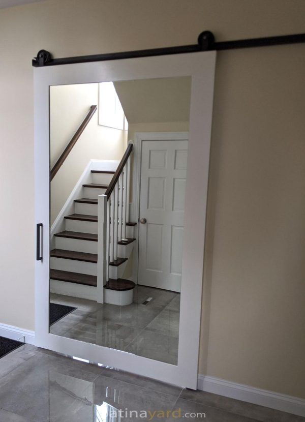White painted wood barn door with a full mirror reflecting a staircase