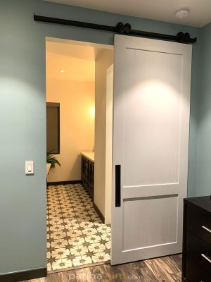 White Wood Shaker Paneled Barn Door White 2 panel shaker barn door opening to a bathroom with patterned tile