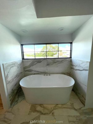 Black metal and glass exterior window above a freestanding tub in a marble bathroom