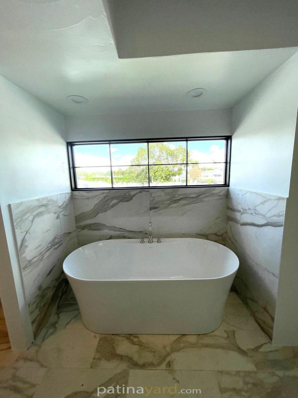 Black metal and glass exterior window above a freestanding tub in a marble bathroom