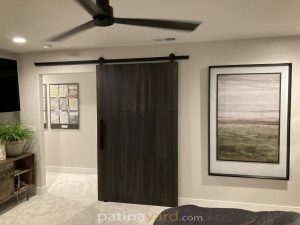 Metal Panel Barn Door Single dark metal panel barn door in a living room with a ceiling fan