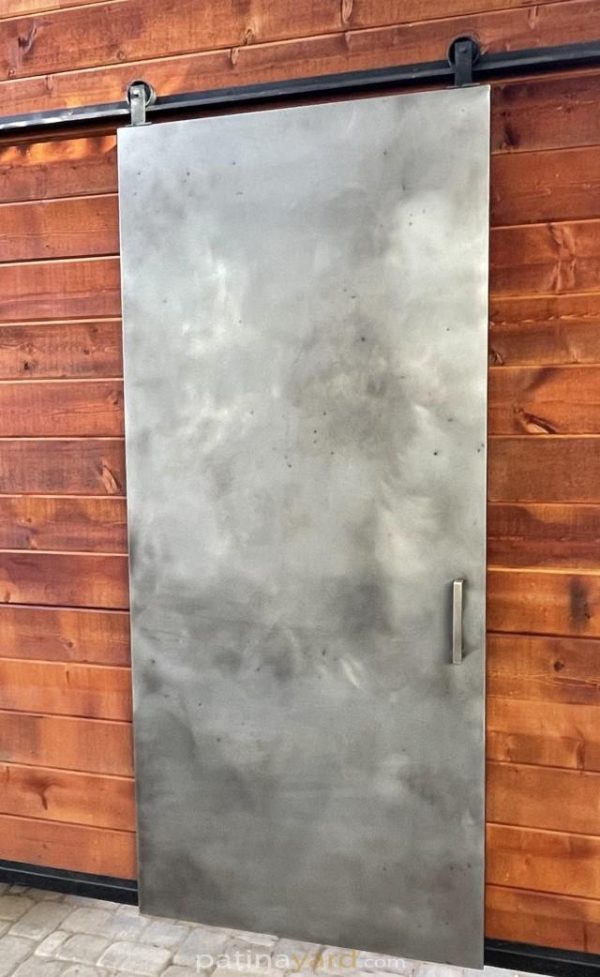 Stainless steel metal panel barn door against a reclaimed wood wall