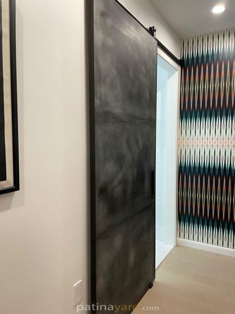 Zinc metal panel barn door with a dark finish in a hallway with patterned wallpaper