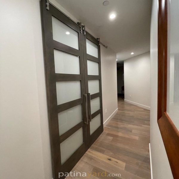 Pair of stained wood barn doors with five satin glass panels each and stainless steel hardware in a hallway
