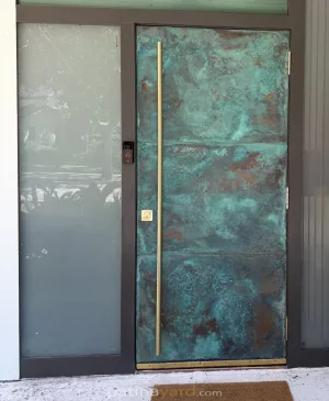 Copper Front Exterior Door Patina copper front door with a tall brass handle beside a frosted glass sidelight