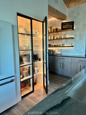 Black steel and glass pantry doors opening to lit pantry shelves