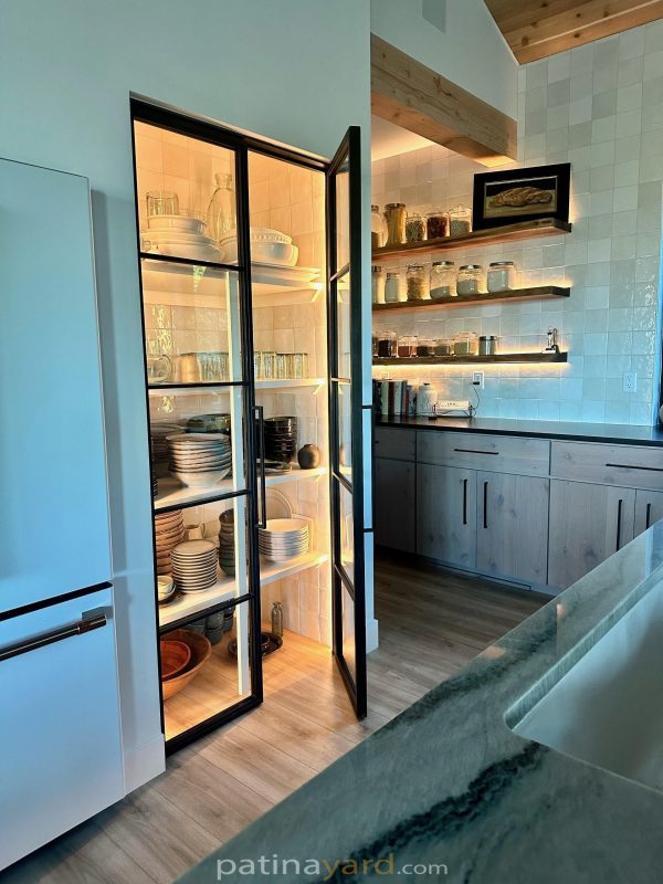 Black steel and glass pantry doors opening to lit pantry shelves