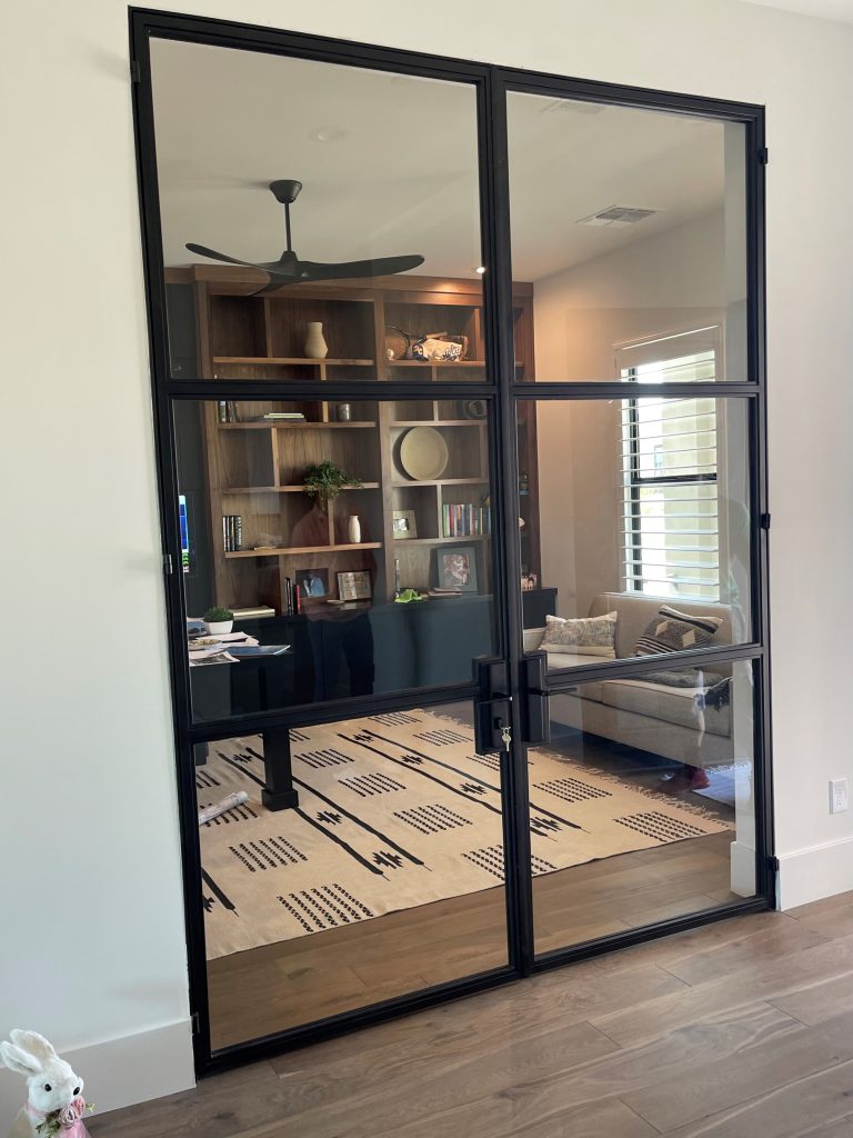 Double black metal and glass doors with clear glass opening to a home den with bookshelves