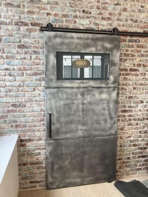 Jen Yanow Zinc barn door with a small window mounted on a brick wall