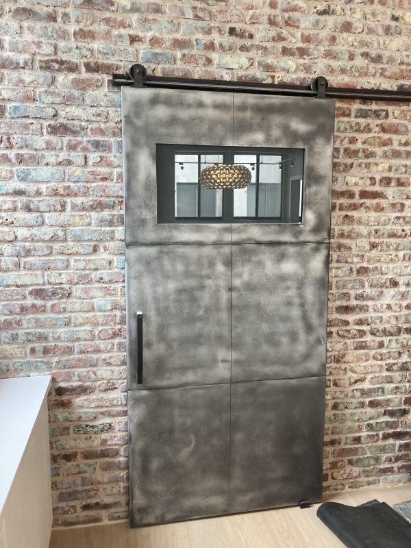 Zinc barn door with a small window mounted on a brick wall