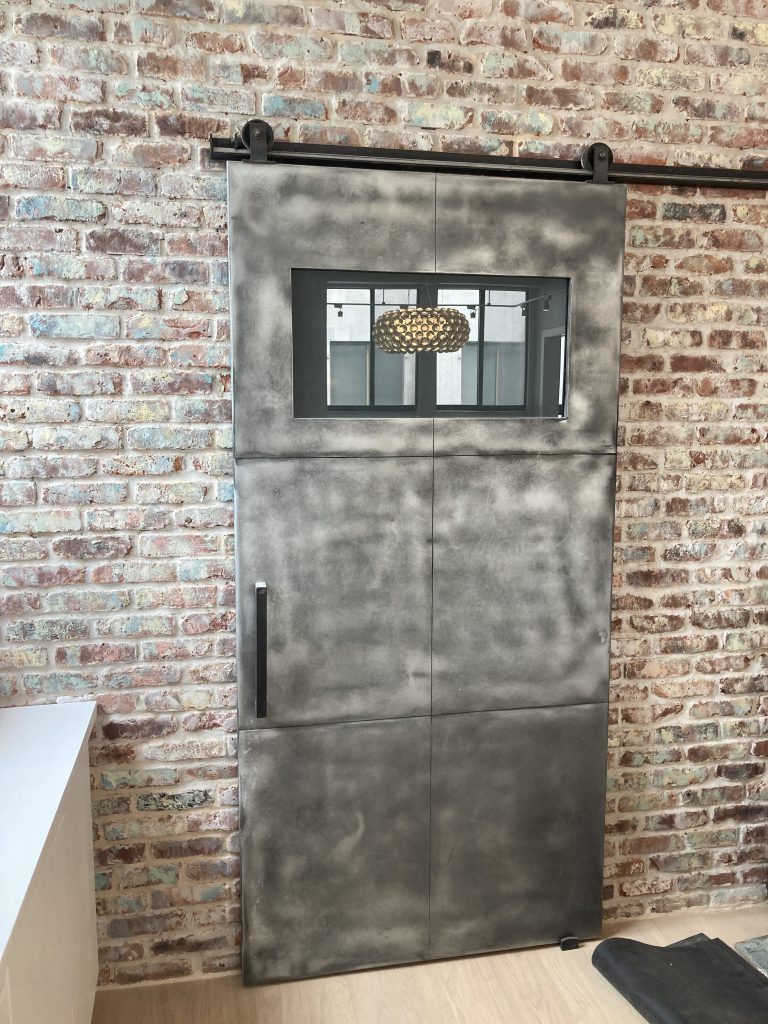 Zinc barn door with a small window mounted on a brick wall