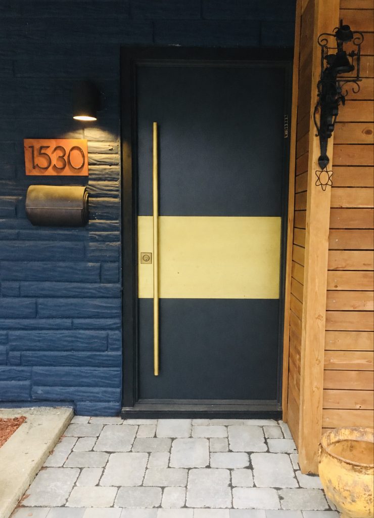 Dark steel front door with a horizontal brass band and a long brass pull