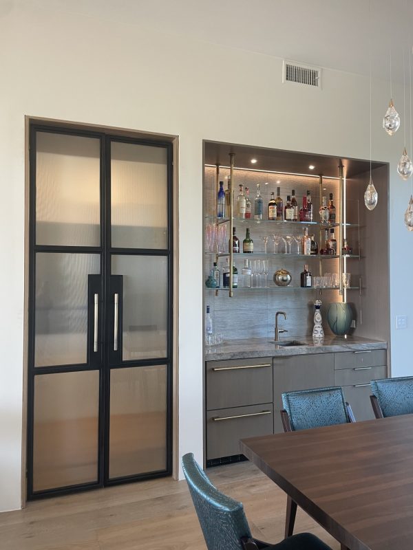 Double reeded glass and black metal doors beside a brass bistro shelf in a home bar