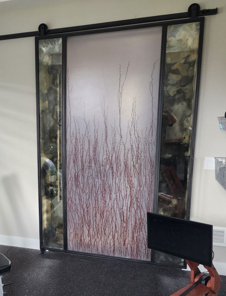 Sliding barn door with a 3form resin tree branch panel and antique mirror side panels in a metal frame