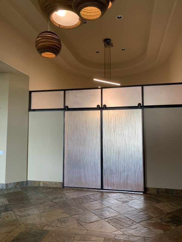 Sliding barn doors with 3form resin panels in black metal frames below frosted transoms