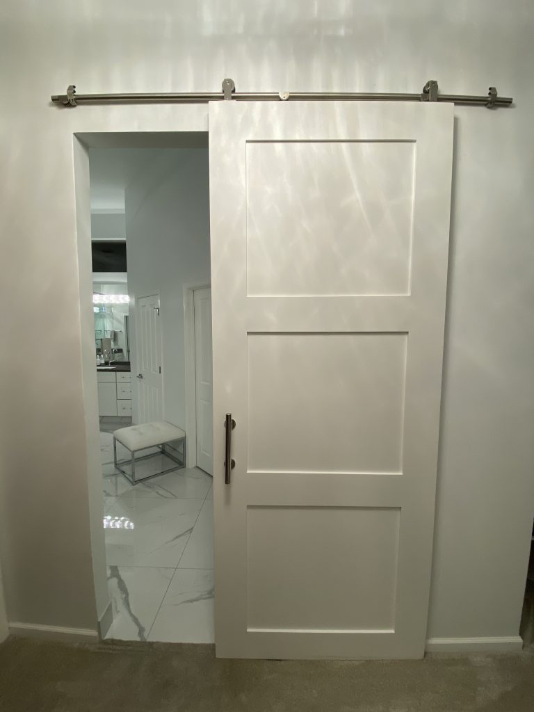 White 3 panel painted shaker barn door opening to a marble bathroom