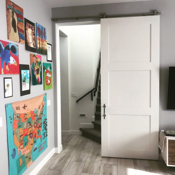 White 3 panel shaker barn door beside a wall of colorful artwork