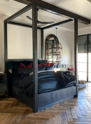 Black metal four poster canopy bed frame on a herringbone wood floor