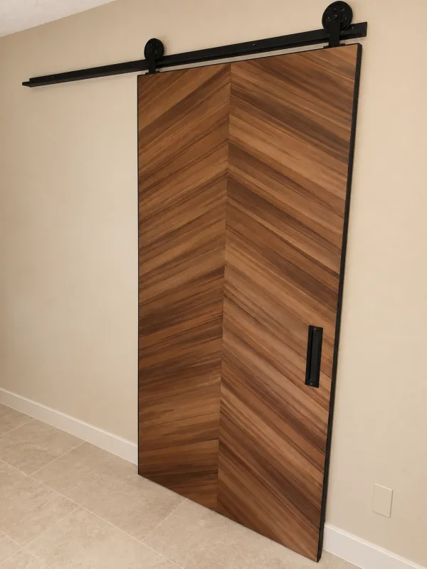 Wood laminate barn door in a chevron pattern with a black track and handle