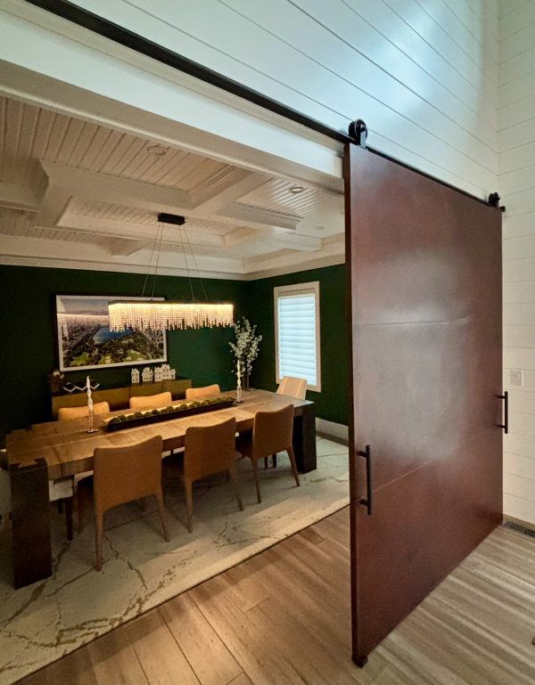 Oversized rust toned patina metal panel barn door sliding open to a dining room with green walls