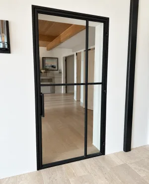 Minimalist black framed metal and glass hinged door in a white wall