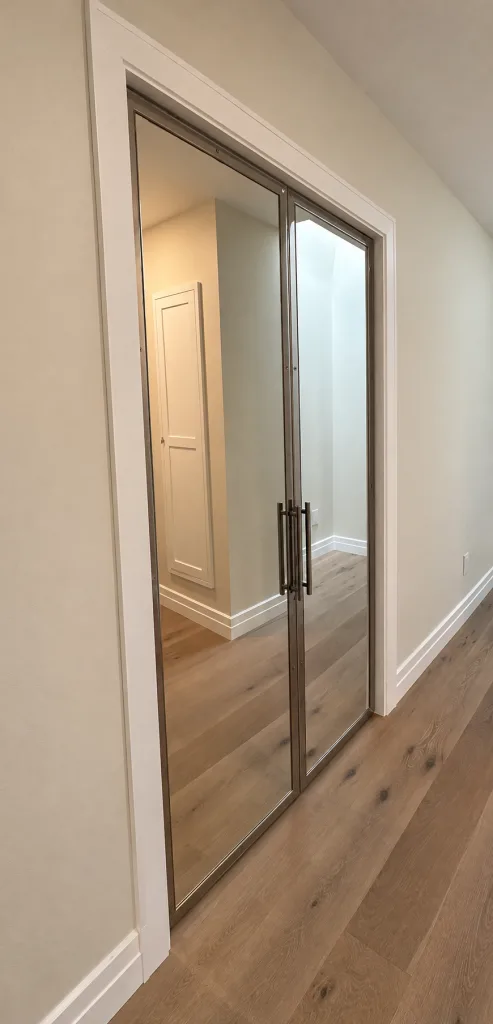 Pair of stainless steel framed mirror pivot closet doors in a hallway