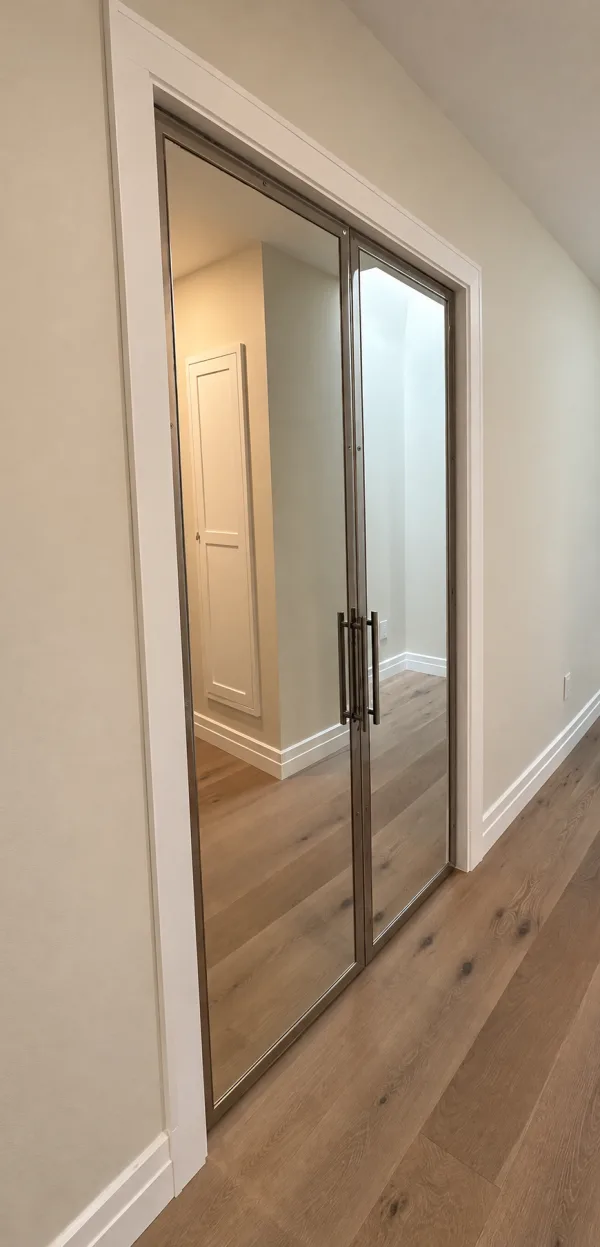 Pair of stainless steel framed mirror pivot closet doors in a hallway