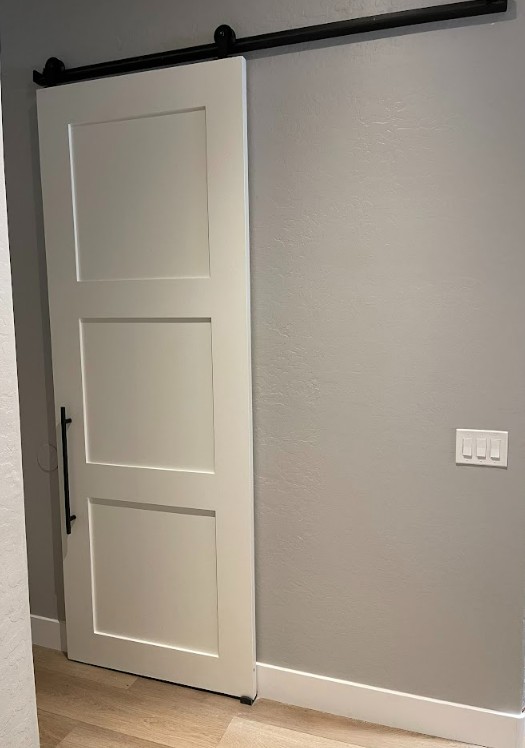 White 3 panel shaker barn door with a long black handle and black hardware