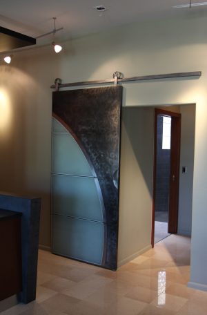 Artistic Metal and Satin Glass Barn Door Patina metal and satin glass sliding barn door with an arched cut out on a stainless steel track