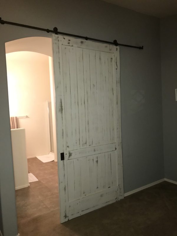 Weathered white painted wood barn door on a black track