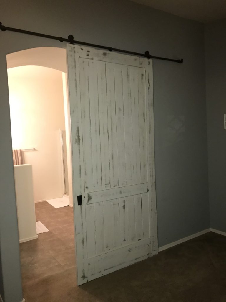 Weathered white painted wood barn door on a black track