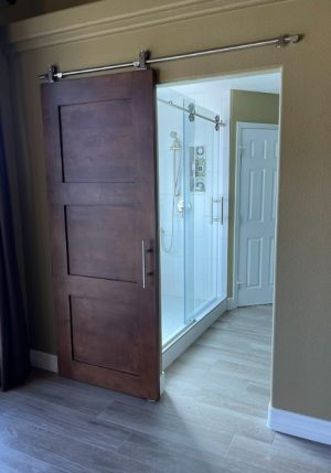 Alder Stained Wood Barn Door Stained alder 3 panel barn door on a stainless track opening to a bathroom