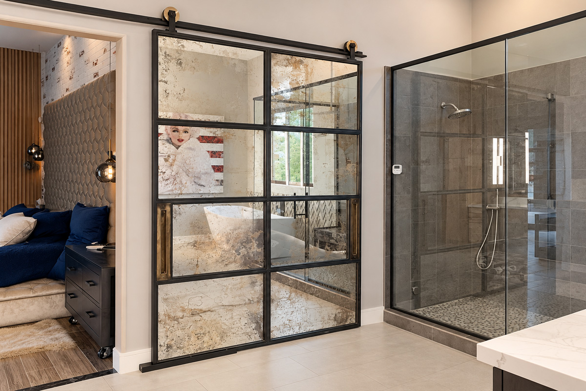 Antique mirror sliding barn door in a black steel frame next to a glass shower