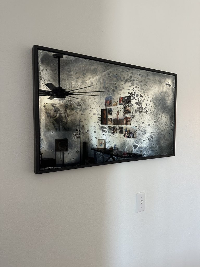 Artistic antique mirror in a black frame on a white wall
