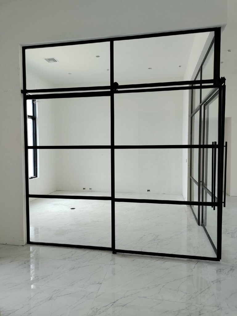Corner black metal and glass enclosure with sliding barn doors and transoms