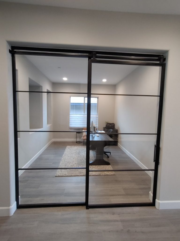 Fixed metal and glass panel beside a sliding black metal and glass barn door to a home office