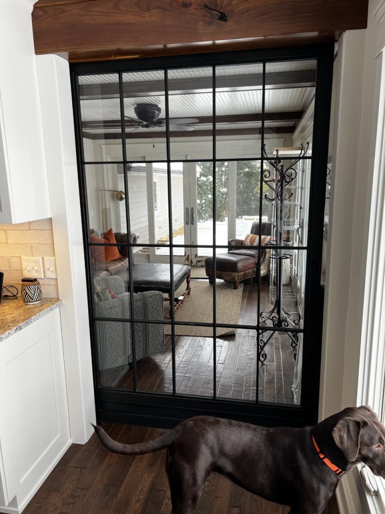 Black metal grid and clear glass barn door opening to a living room