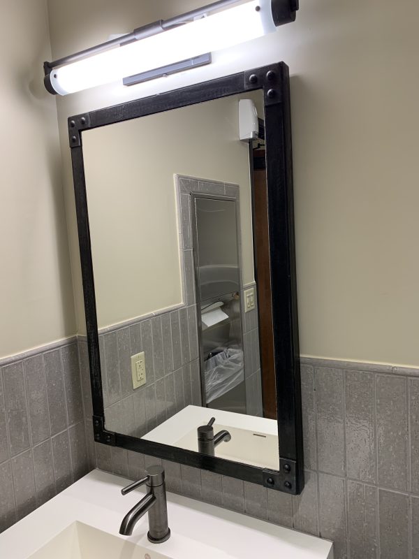 Industrial framed mirror with rivets above a bathroom sink