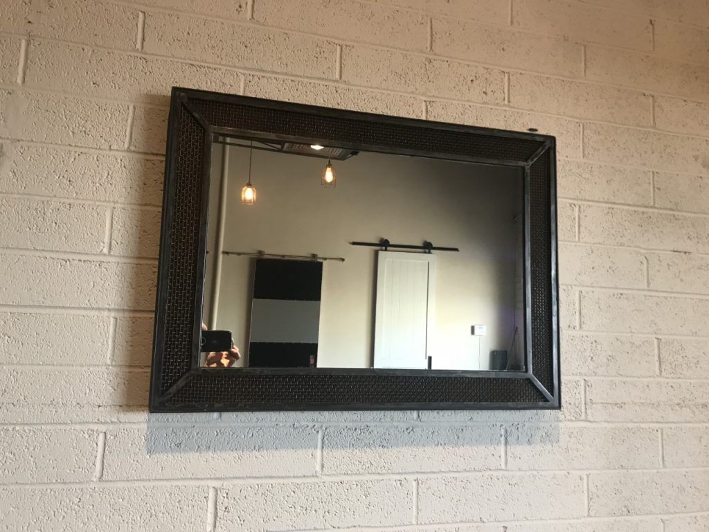 Industrial metal and mesh framed mirror on a white brick wall