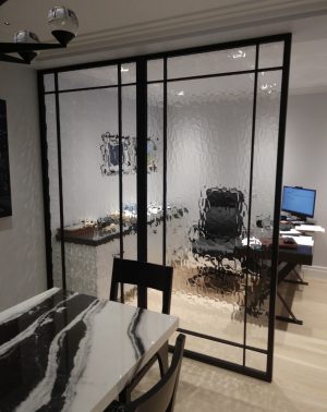 Black metal and clear glass room divider between a dining area and an office