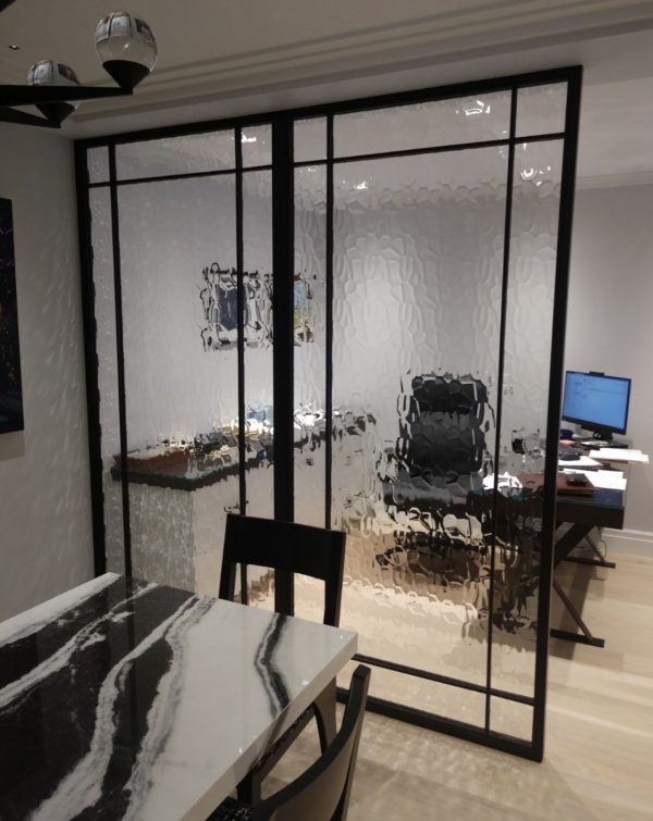 Black metal and clear glass room divider between a dining area and an office
