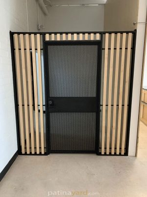 Black metal security gate with a perforated steel door and wood slat sides in a commercial space