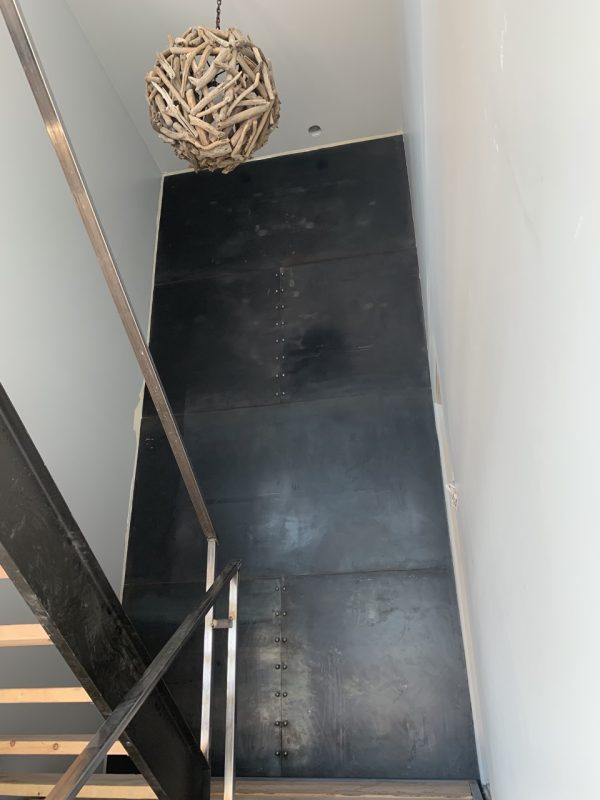Tall blackened steel accent wall along a staircase