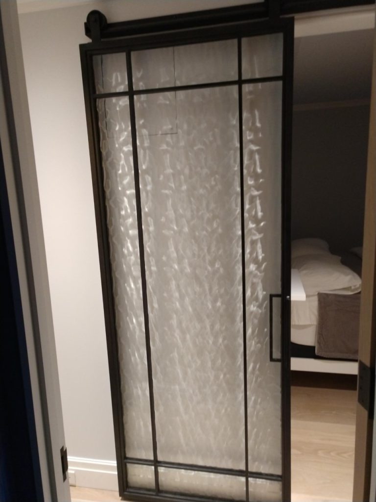 Black metal barn door with textured specialty glass at a bedroom entry