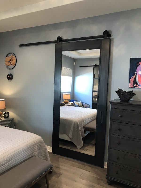 Black metal panel barn door with a large mirror inset on a sliding track in a bedroom
